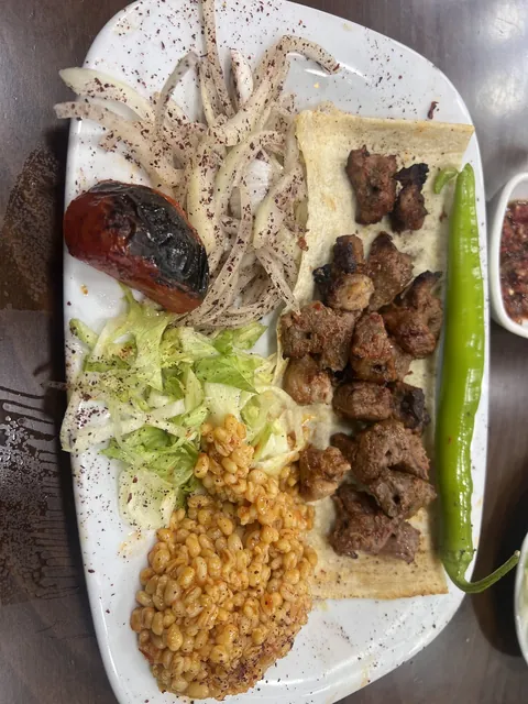 Beyaz tabakta kuzu şiş, bulgur pilavı ve közlenmiş domates